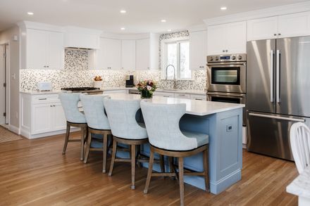 Bright white kitchen with blue island stools, stainless appliances, and hardwood floors
