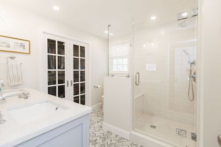 Bright white bathroom with double vanity, glass shower, and French doors