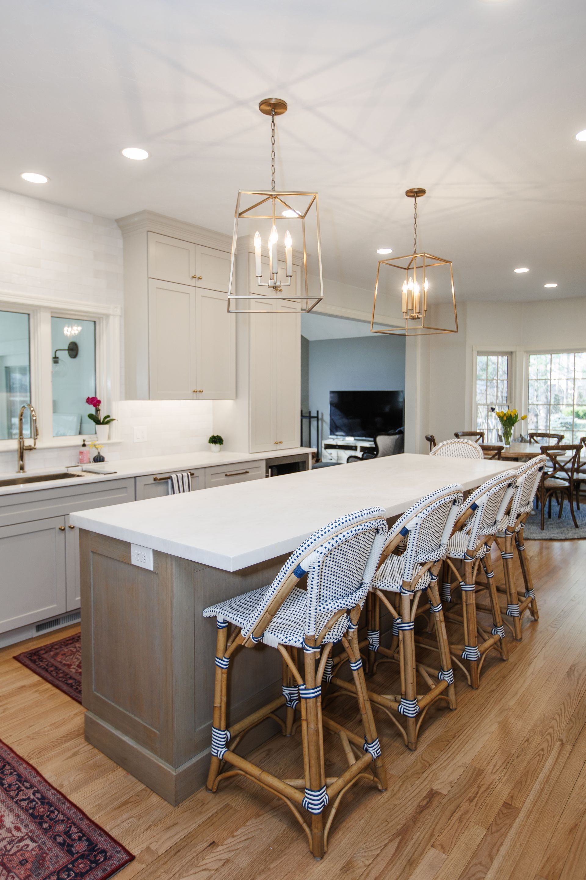 Bright modern kitchen with a large island, wooden stools, pendant lights, and white cabinetry