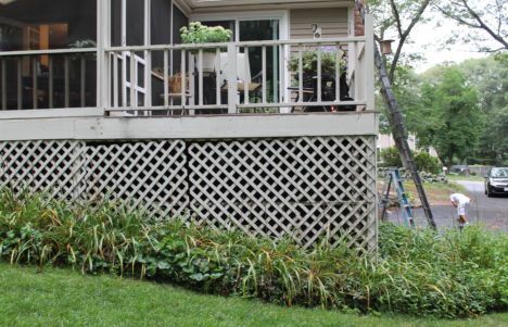 Porch and lattice skirting on a raised house beside a grassy yard, with a person in the background