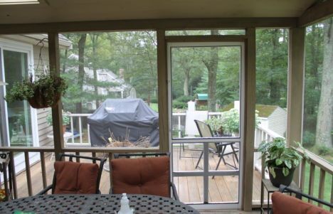 Screened porch with patio furniture overlooking a backyard deck and a covered grill.
