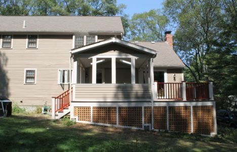 Back of beige house with a screened porch, red deck railings, and a grassy yard
