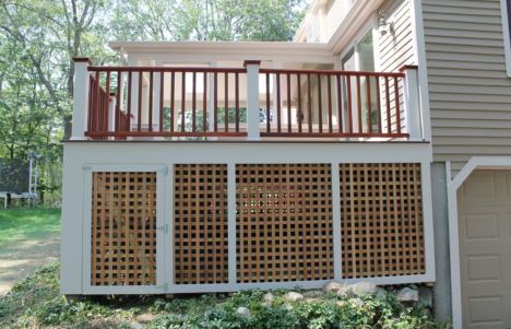 Wooden deck above a lattice-enclosed patio beside a house, with trees in the background.
