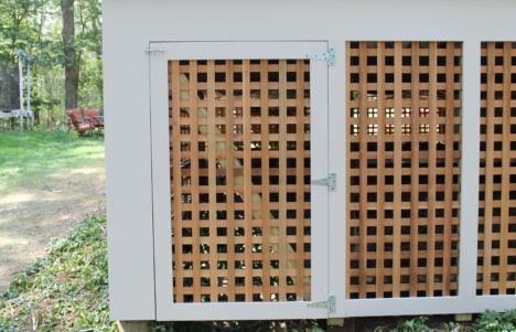 White outdoor enclosure with two wooden lattice doors beside a grassy yard and trees