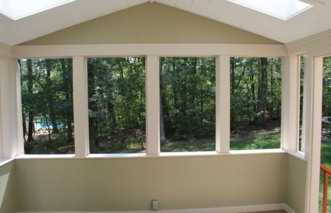Bright sunroom with beige walls, skylights, and large windows overlooking trees and greenery.