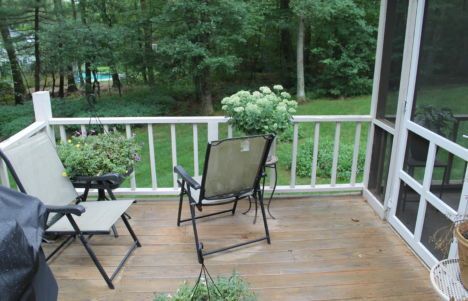 Wooden porch with two folding chairs overlooking a green wooded yard.