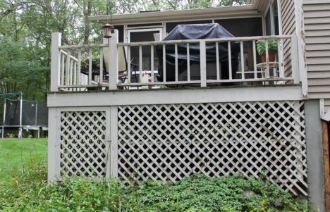 Wooden deck with white lattice skirting and railing in a wooded backyard