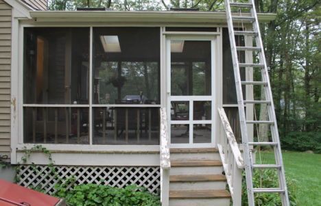 Screened porch with stairs and a ladder on the right, set among trees.
