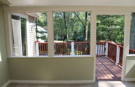 Sunroom with large windows opening to a wooden deck and green trees outside