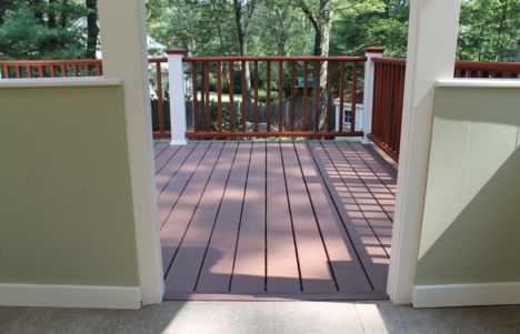 Porch deck with wooden railing and open doorway overlooking trees and a grassy yard