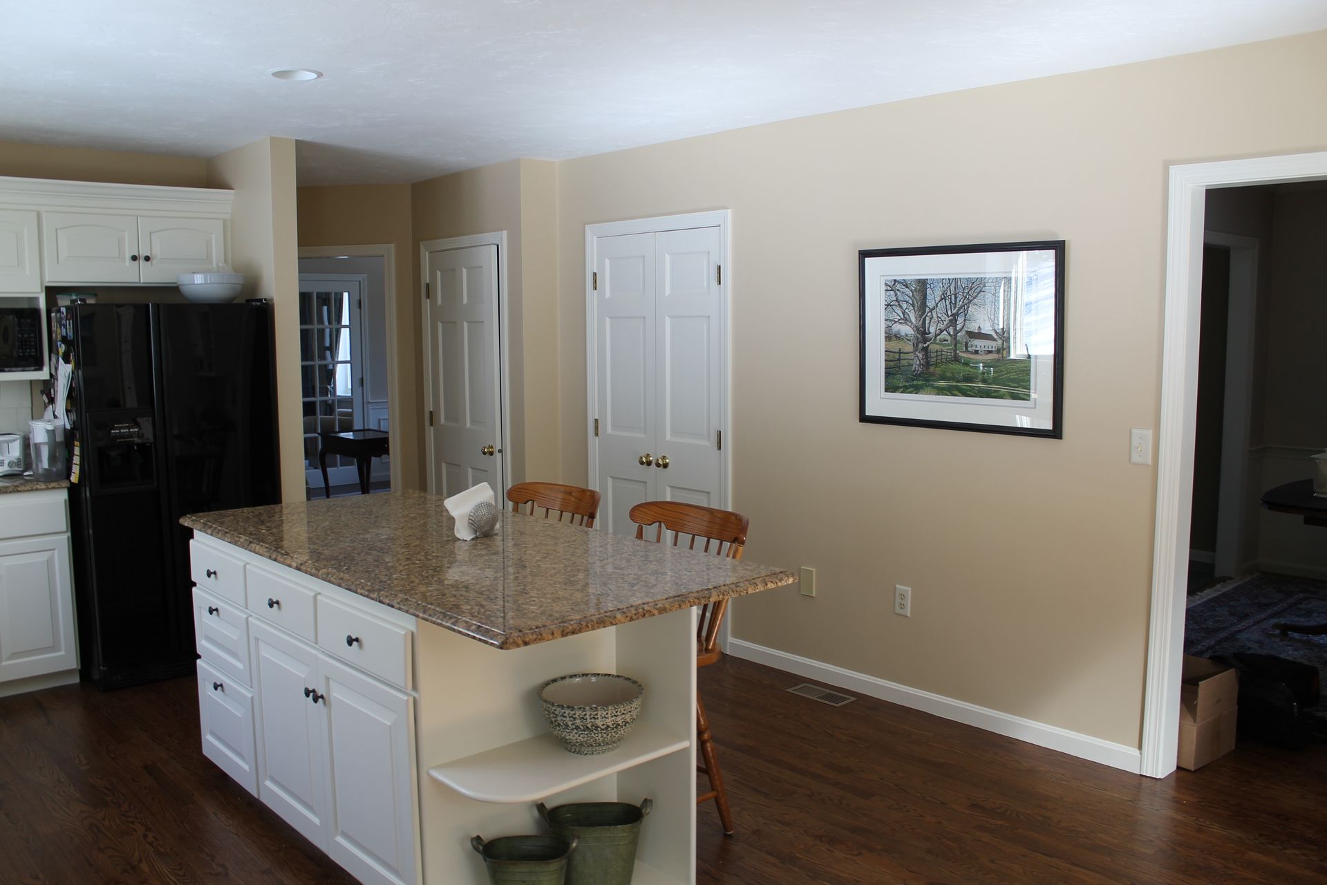 Modern kitchen with granite island, white cabinets, dark wood floors, and framed wall art.