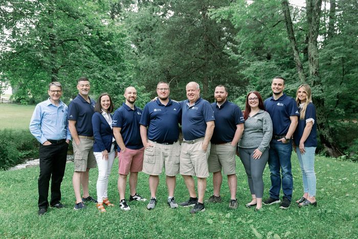 Group of people standing together on a grassy lawn in front of trees outdoors
