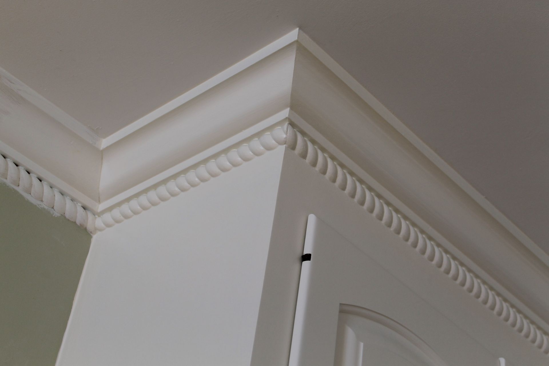 White crown molding and decorative trim at the corner of a beige room, above a white door frame