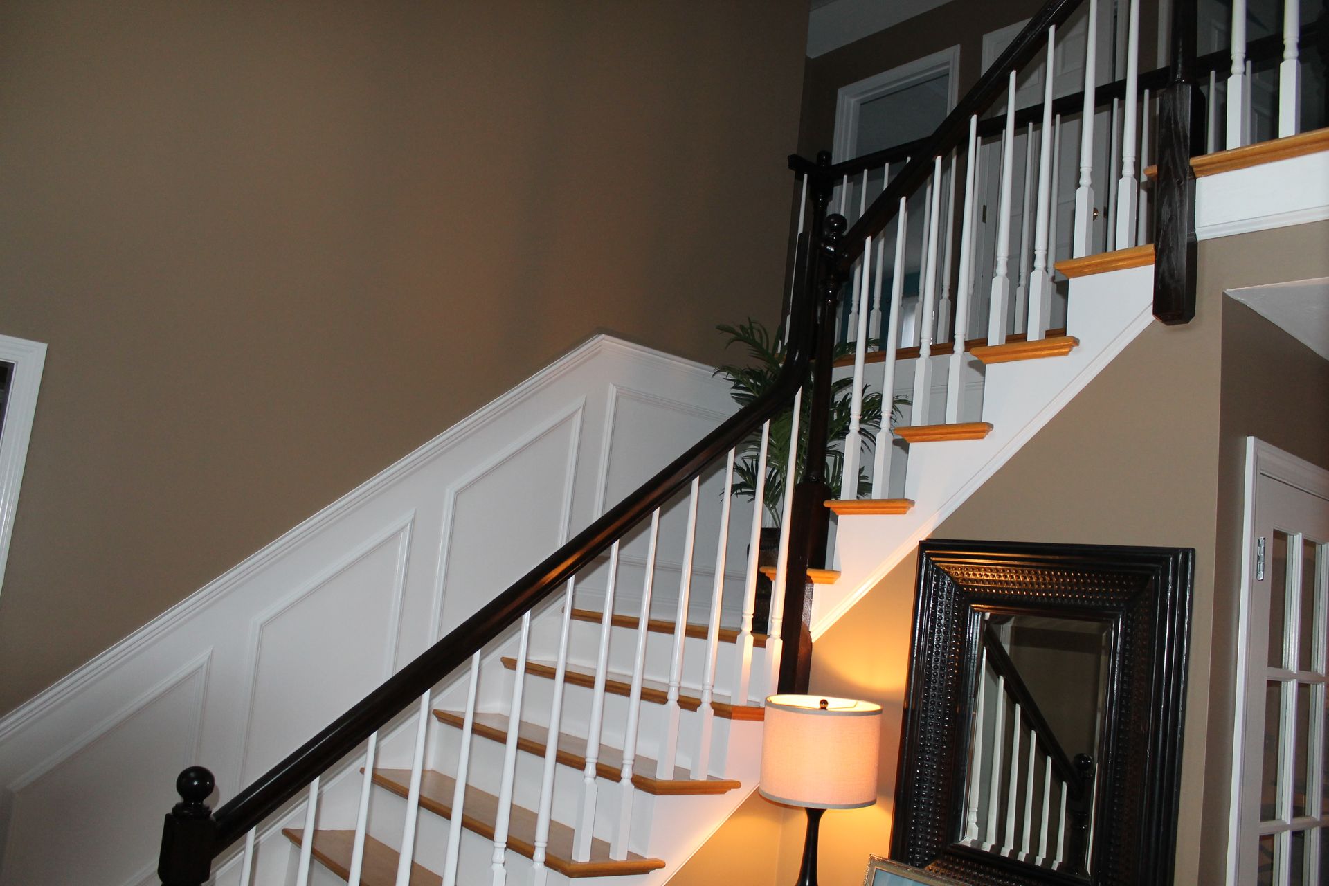 Interior staircase with white railing, dark banister, and a lamp at the base, lit by warm light