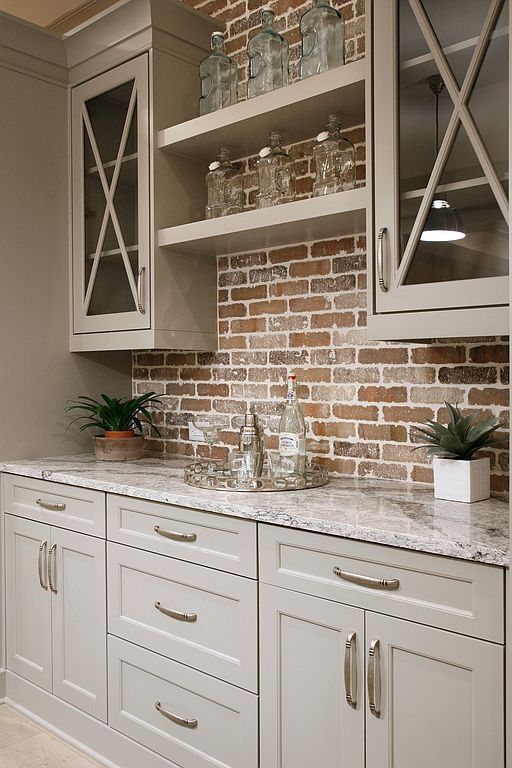 Light gray kitchen cabinets with white marble countertop, open shelves, and exposed brick backsplash