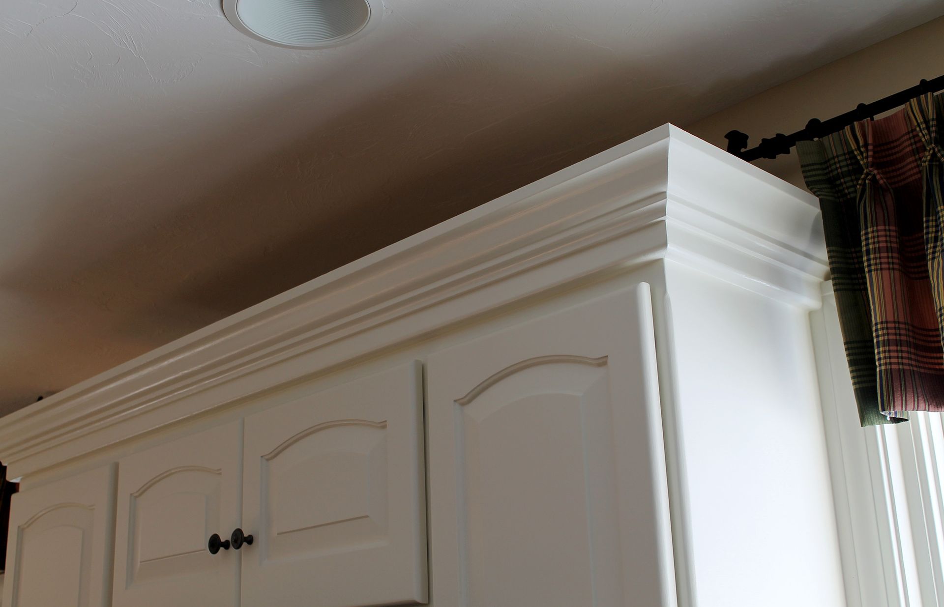 White kitchen cabinet with decorative crown molding near a window and curtains