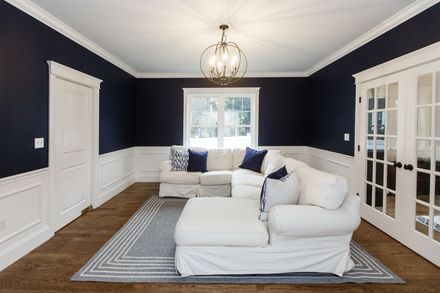 Elegant living room with navy walls, white trim, sectional sofa, rug, and glass French doors