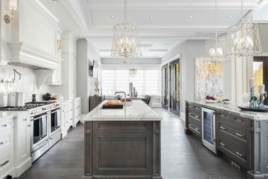 Elegant white kitchen with central island, chandeliers, and dark cabinetry, shown in a bright open layout