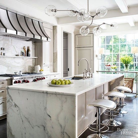 Bright white modern kitchen with marble island, bar stools, and large sunlit windows