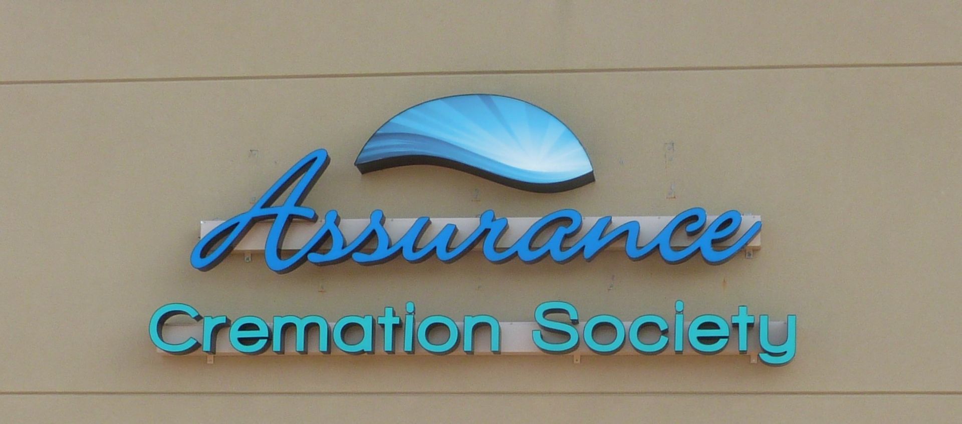 Blue sign reading “Assurance Cremation Society” on a beige wall.