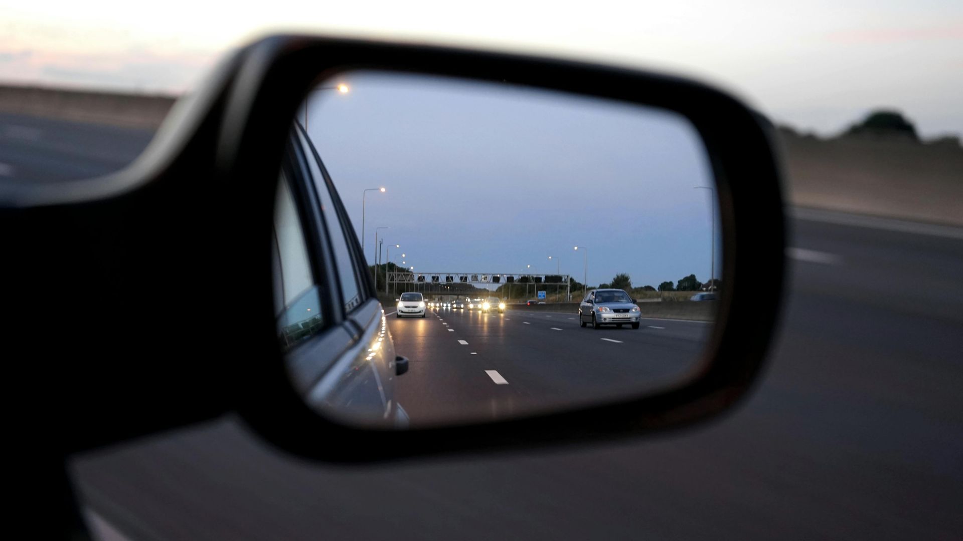Side view mirror showing a highway with cars at dusk — Greenaway's Taxi in Forster, NSW
