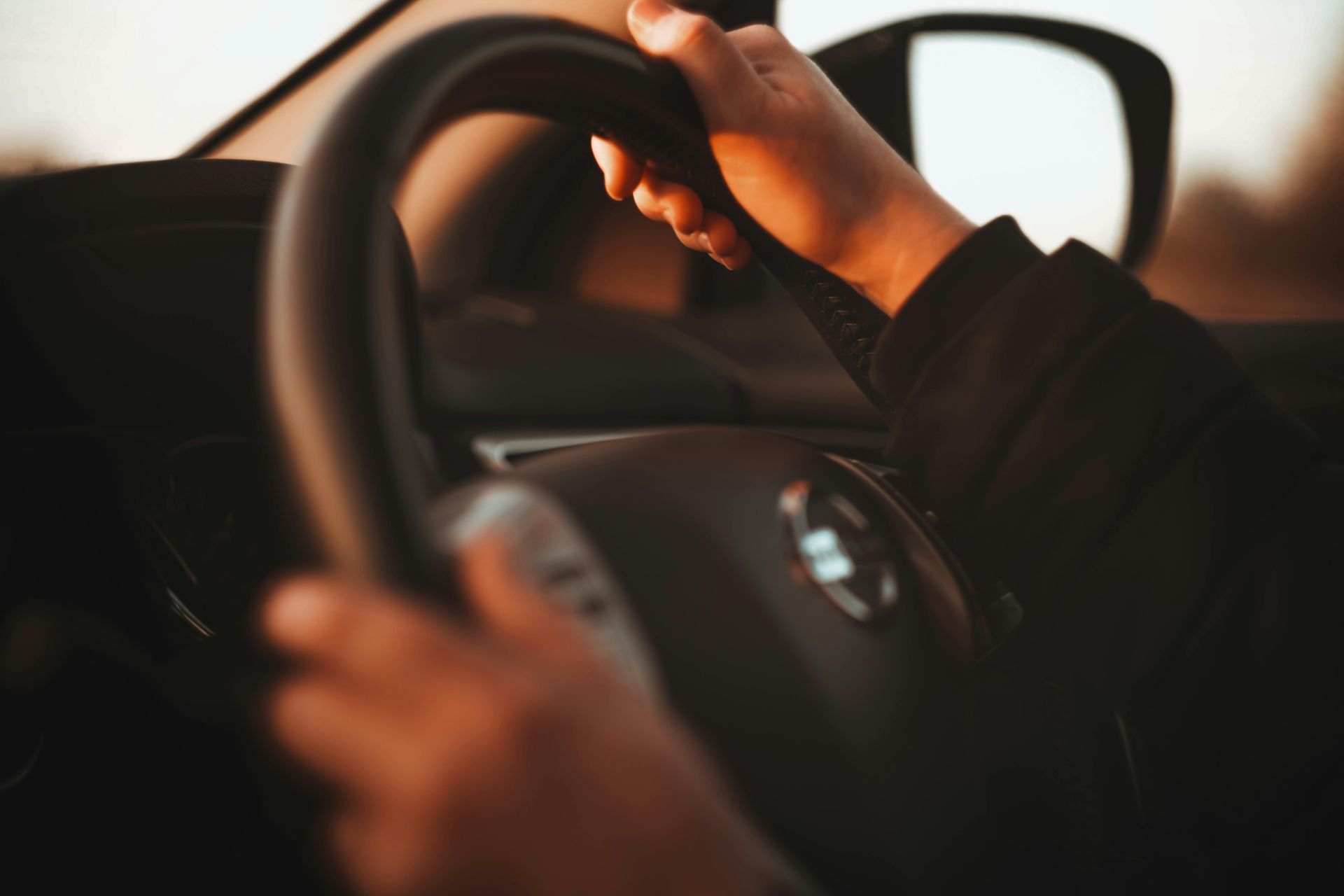 Person's hands holding a car steering wheel, backlit with golden light, driving a vehicle — Greenaway's Taxi in Comboyne, NSW