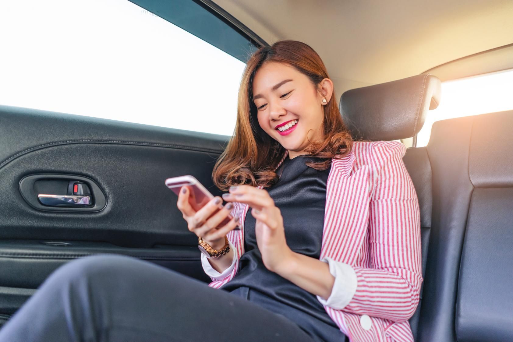 A Woman Is Sitting in The Back Seat of A Car Looking at Her Cell Phone — Greenaway's Taxi in Nabiac, NSW