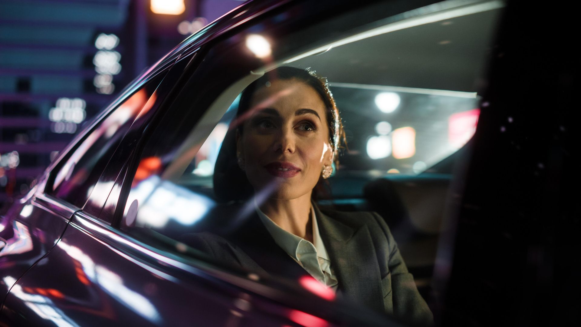 Woman in a dark suit smiles while sitting in a car at night, city lights reflect on the window — Greenaway's Taxi in Lansdowne, NSW