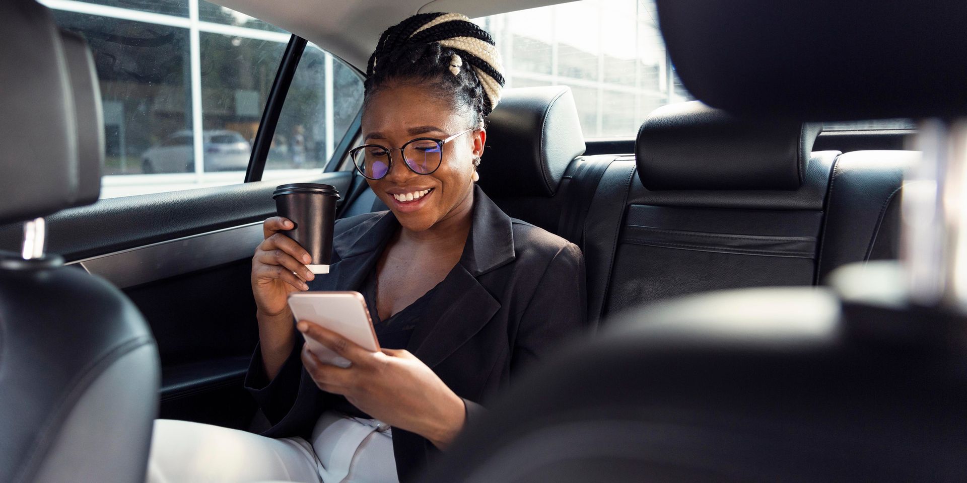 Woman in a car smiling while looking at her phone and holding a coffee cup — Greenaway's Taxi in Wingham, NSW
