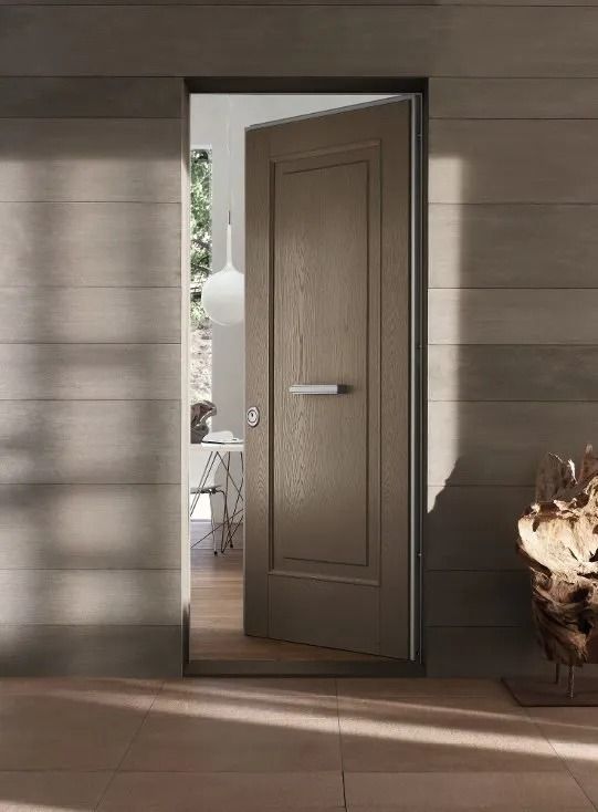 Una porta marrone socchiusa in un interno illuminato dal sole lascia intravedere un luminoso patio esterno.