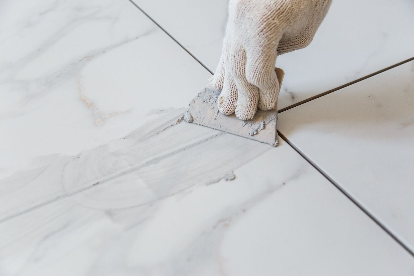 A person is applying grout to a tile floor with a spatula.