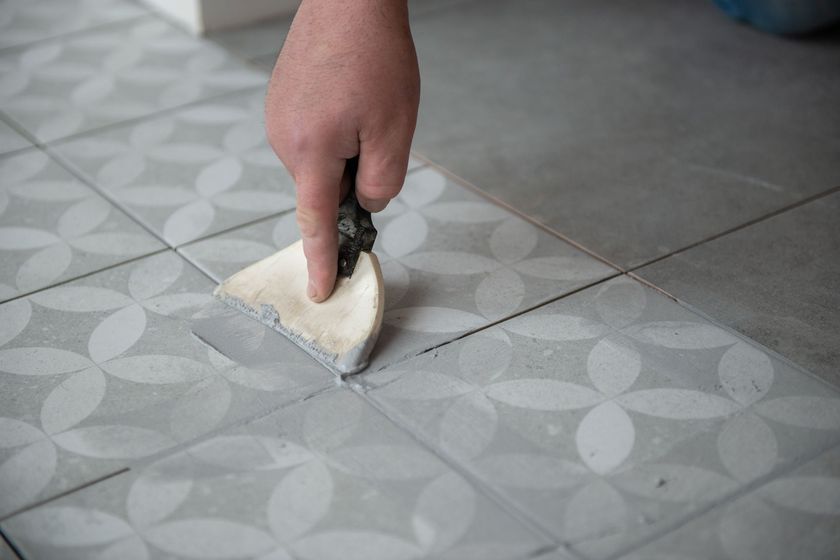 A person is applying grout to a tile floor with a spatula.