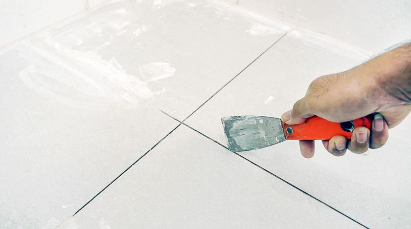 A person is holding a spatula over a tile floor.