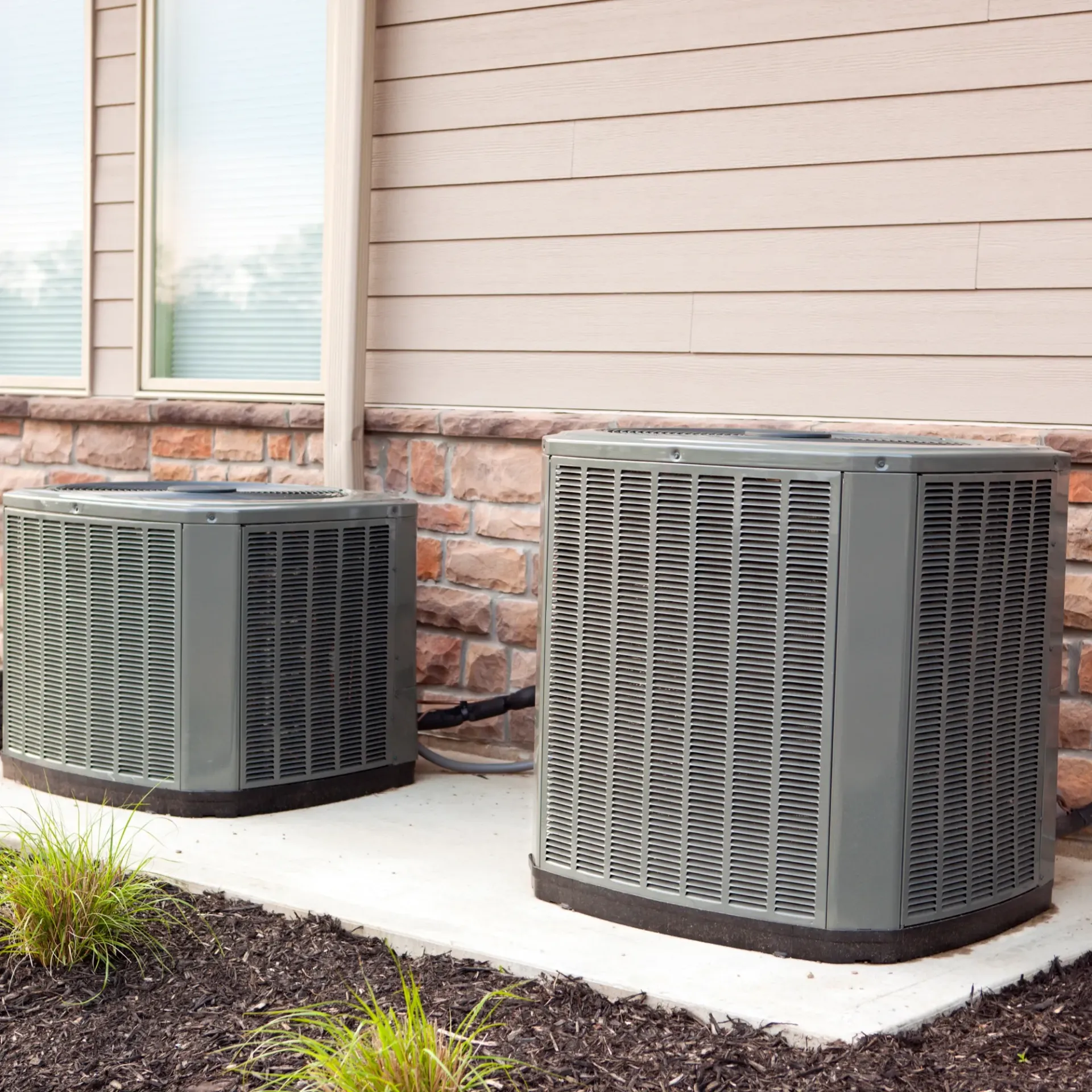 Aarden Air Service Heating & Air Conditioning- Two air conditioners are sitting next to each other on the side of a house.