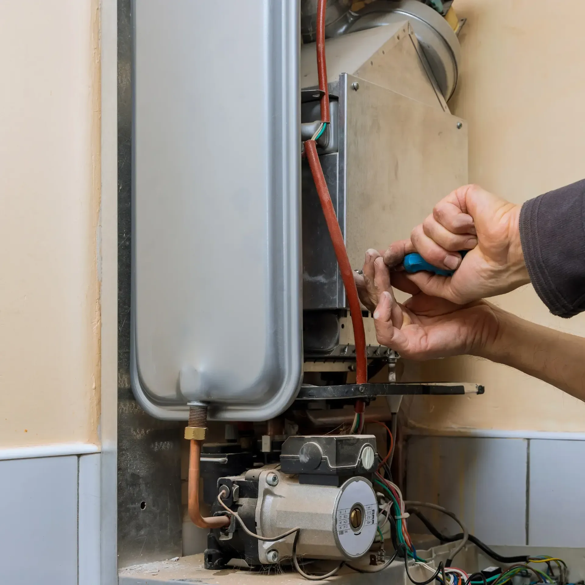 Aarden Air Service Heating & Air Conditioning- A person is fixing a boiler with a screwdriver.