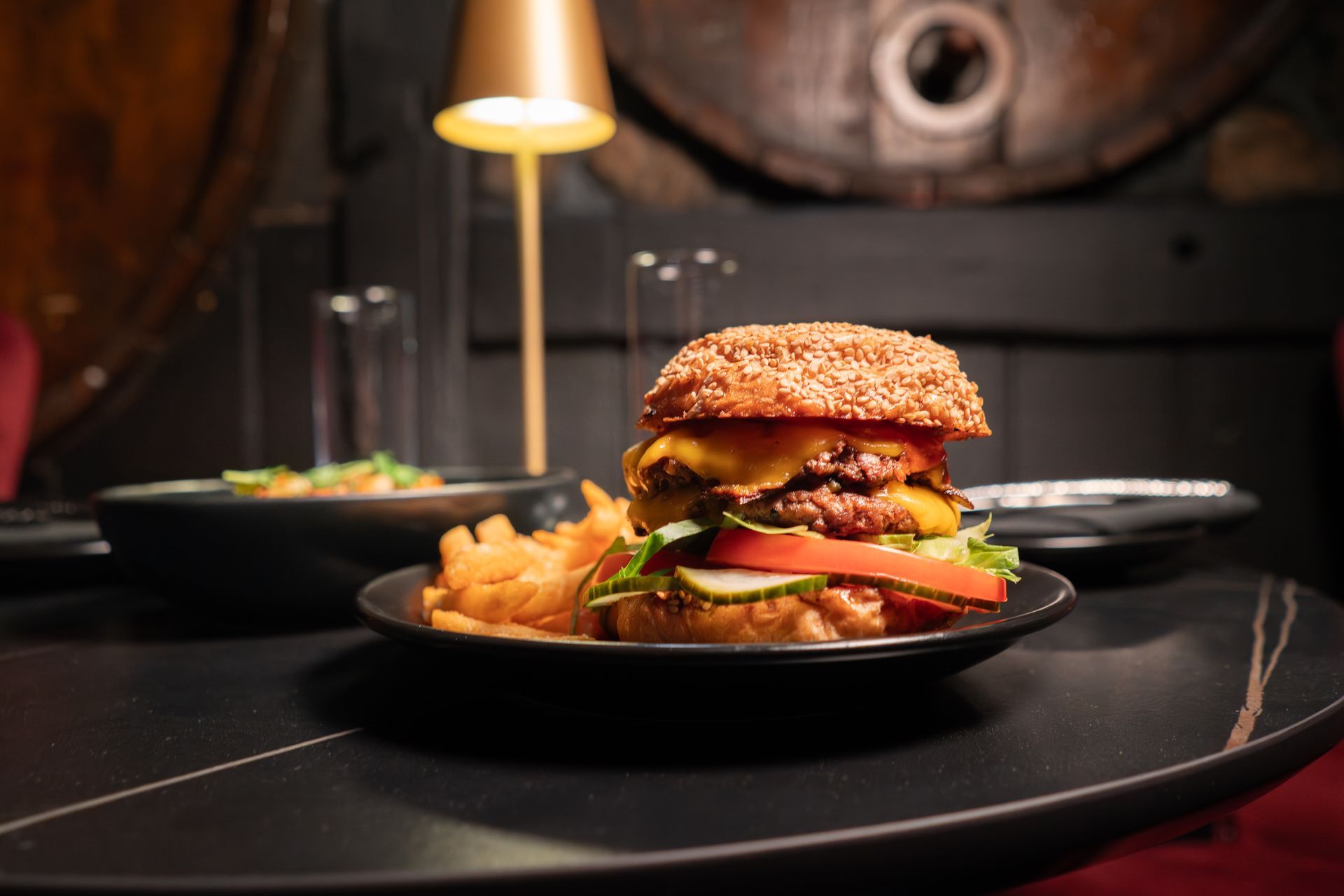 Burger with fries on a black plate in a dimly lit restaurant setting