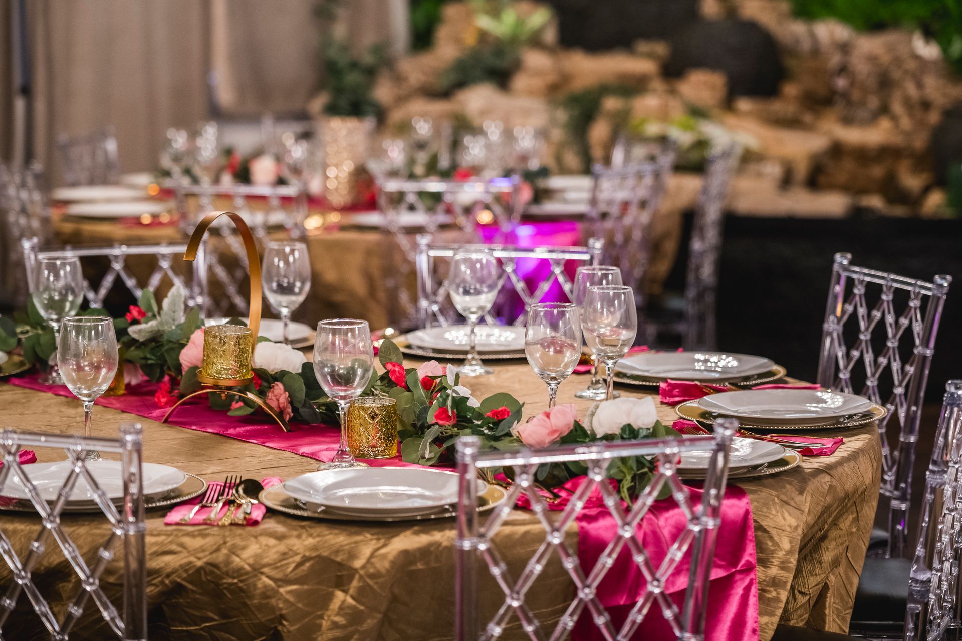 Elegant banquet table with silver chairs, pink napkins, red roses, and lit centerpiece in a dim ballroom