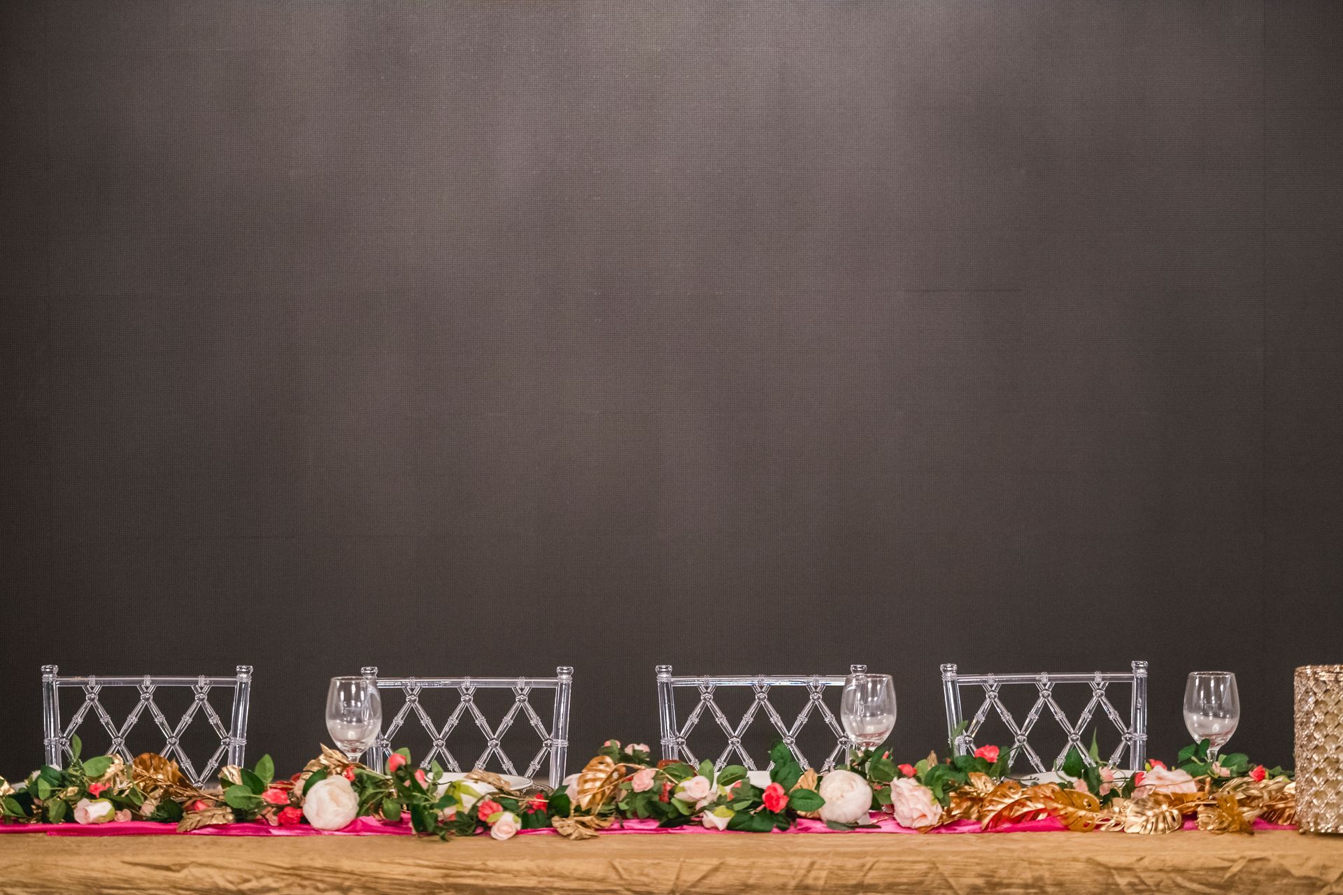 Decorated banquet table with flowers, candles, and white lattice chair backs against a dark backdrop