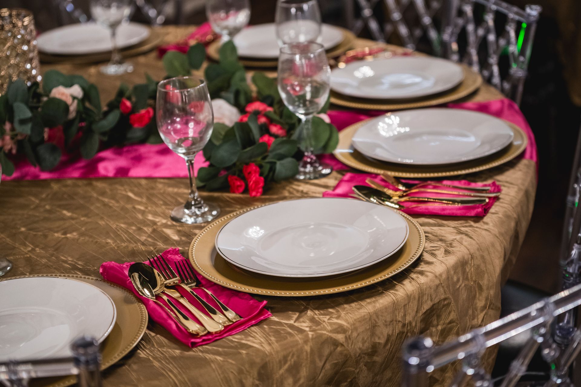 Elegant banquet table set with gold chargers, white plates, pink napkins, and wine glasses