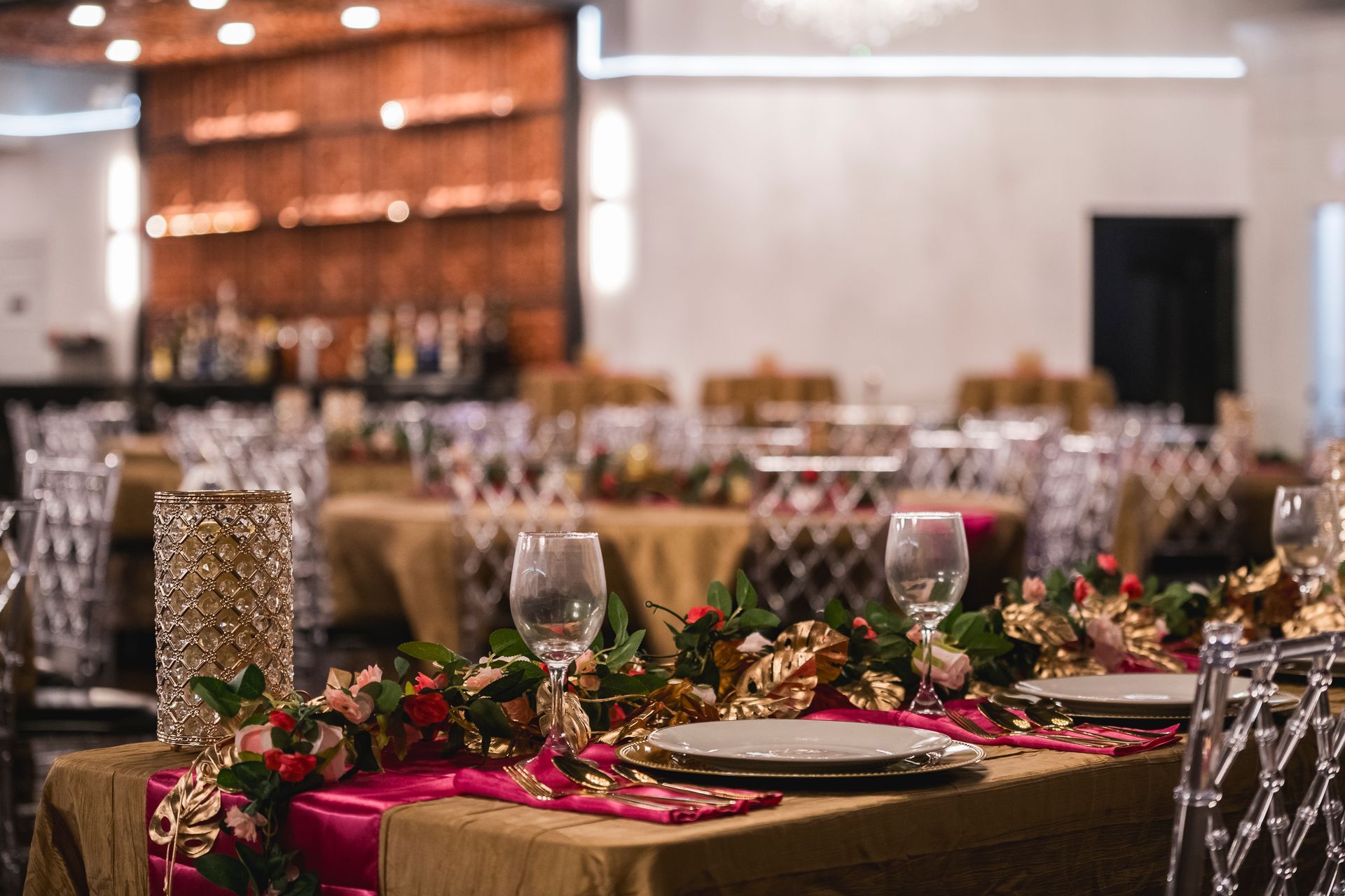 Decorated banquet table with pink runner, flowers, candles, and glassware in a softly lit event hall