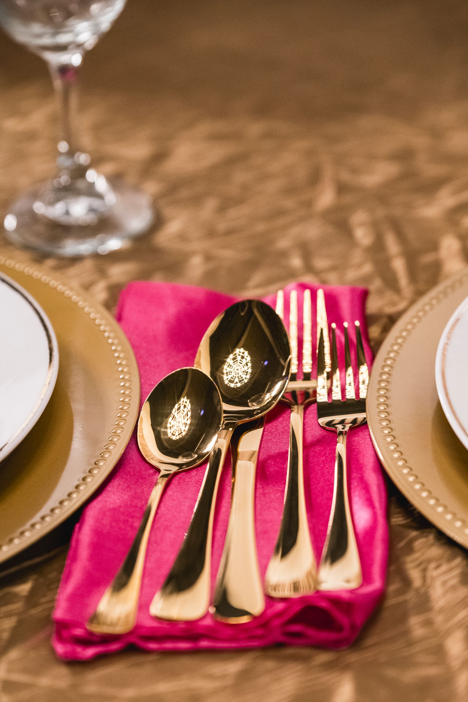 Gold silverware on a bright pink napkin at a formal table setting