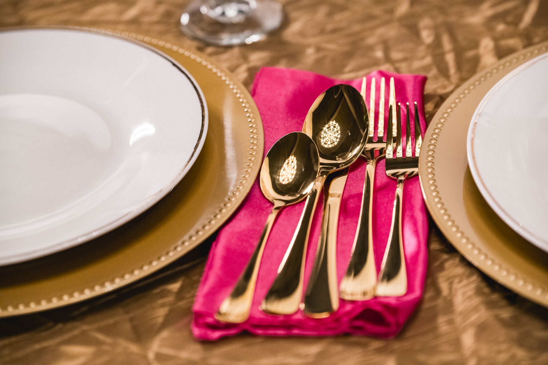Elegant table setting with gold-rimmed plates, pink napkin, and gold utensils on a gold tablecloth