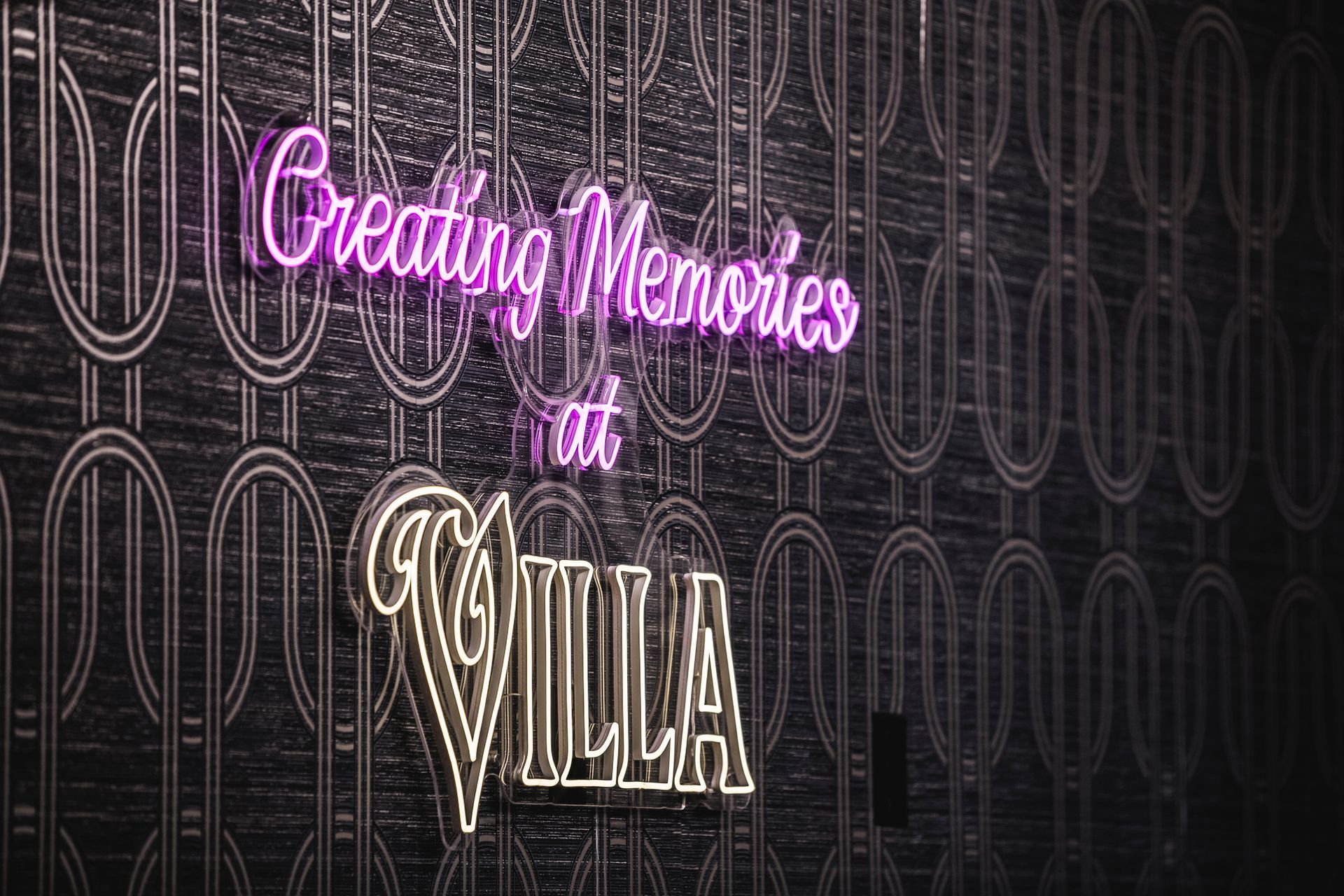 Neon sign reading “Creating Memories at Villa” on a dark patterned wall
