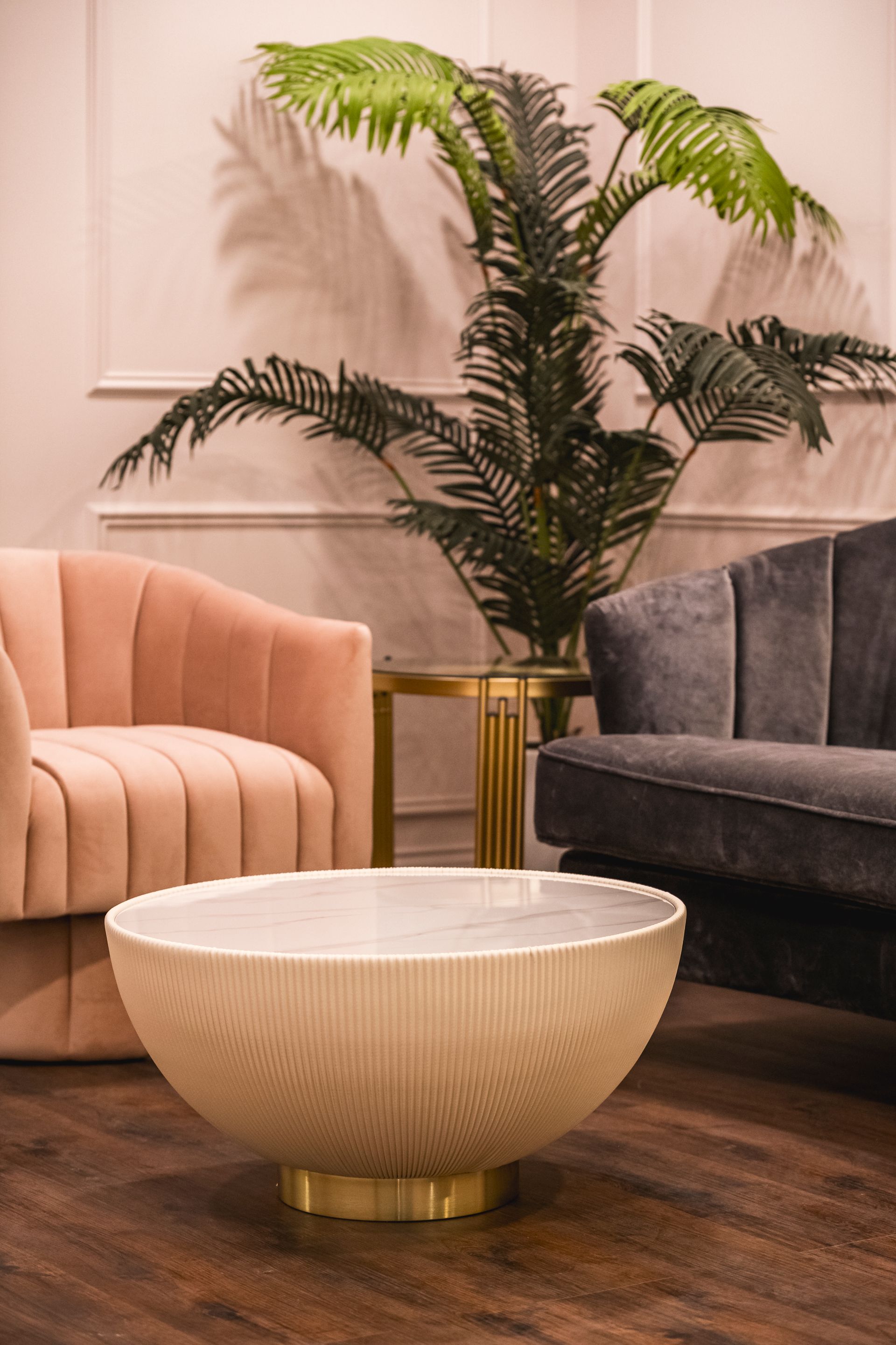 Modern living room with a pink chair, dark sofa, white coffee table, and tall potted palm plant.