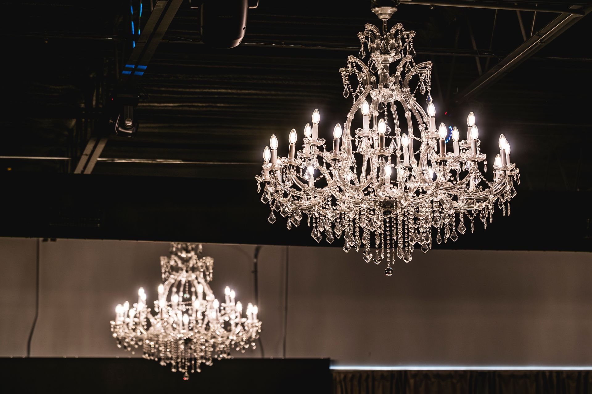 Two ornate crystal chandeliers hanging from a dark ceiling in a dimly lit room