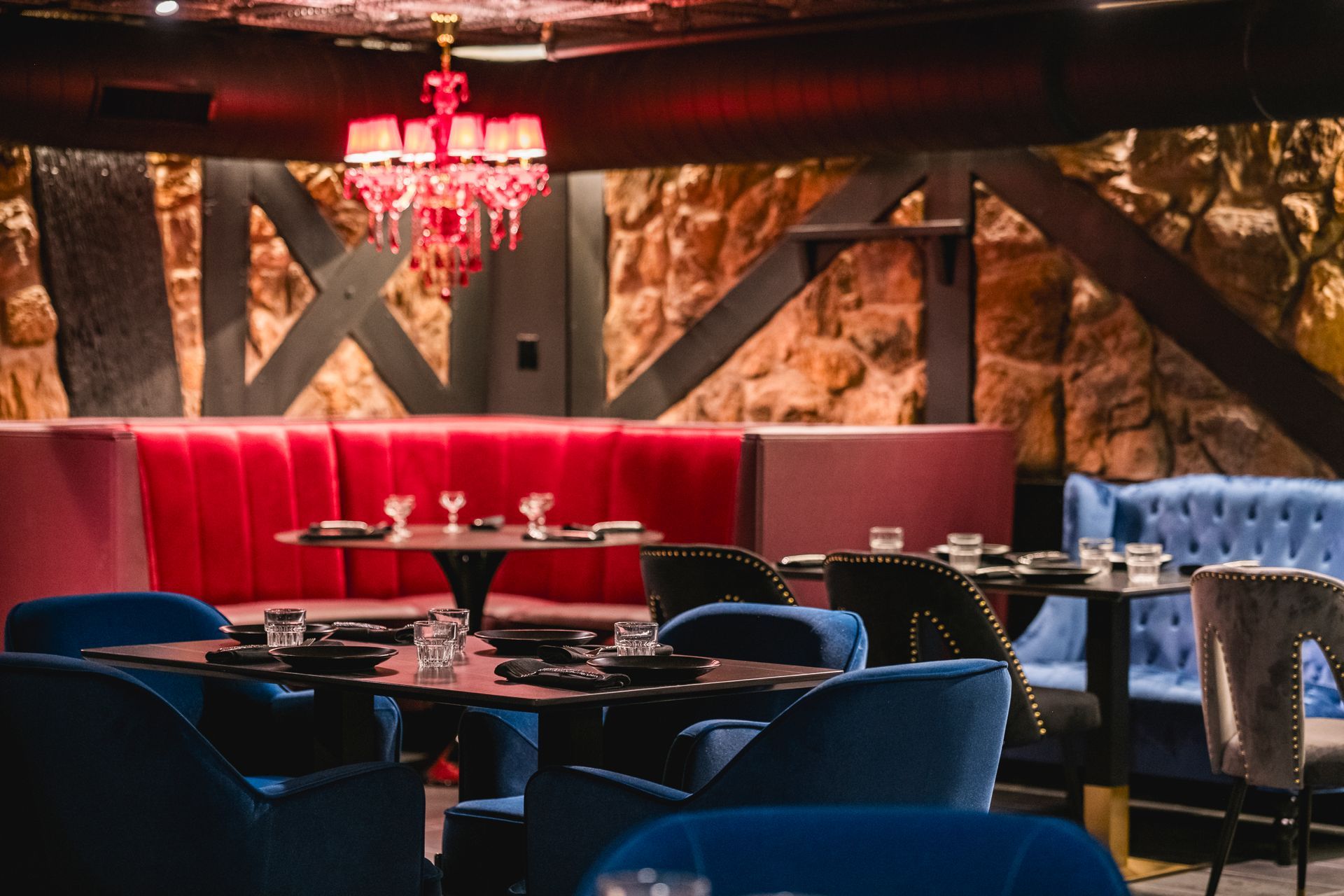 Dimly lit lounge with blue chairs, red booths, a chandelier, and rustic wood-and-stone decor