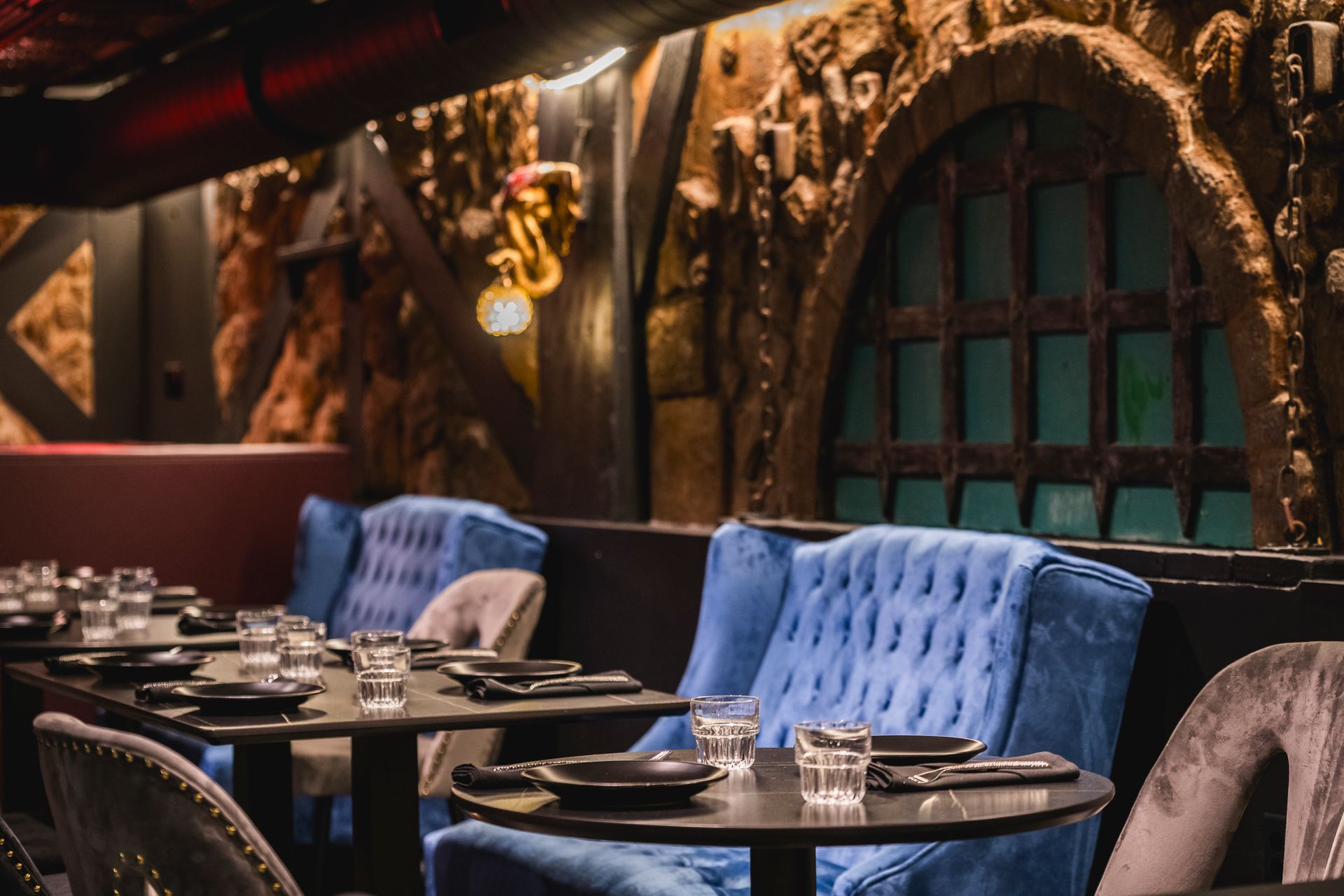 Elegant lounge with blue velvet chairs, small tables, and ornate arched decor in warm lighting