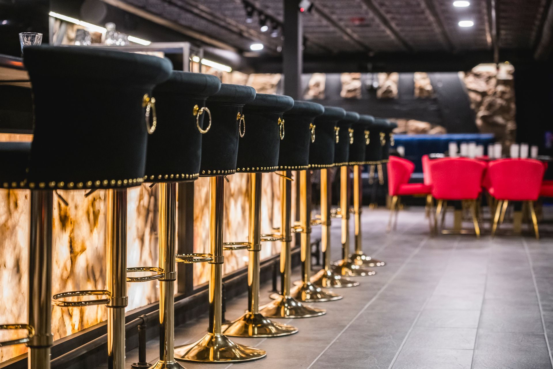 Row of black and gold barstools at a modern bar with red chairs in the background