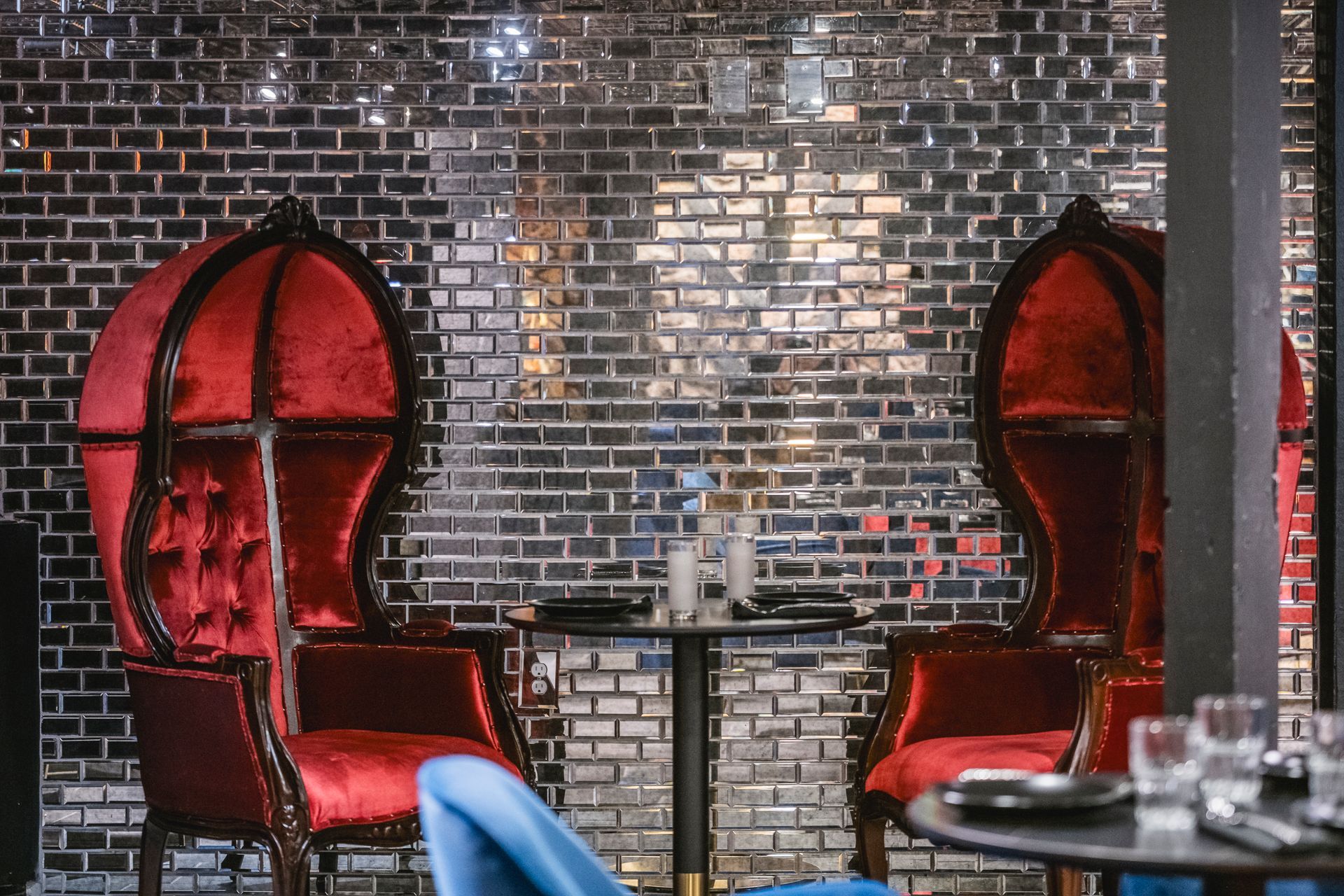 Red velvet booth seating around a small table against a dark brick wall in a restaurant.