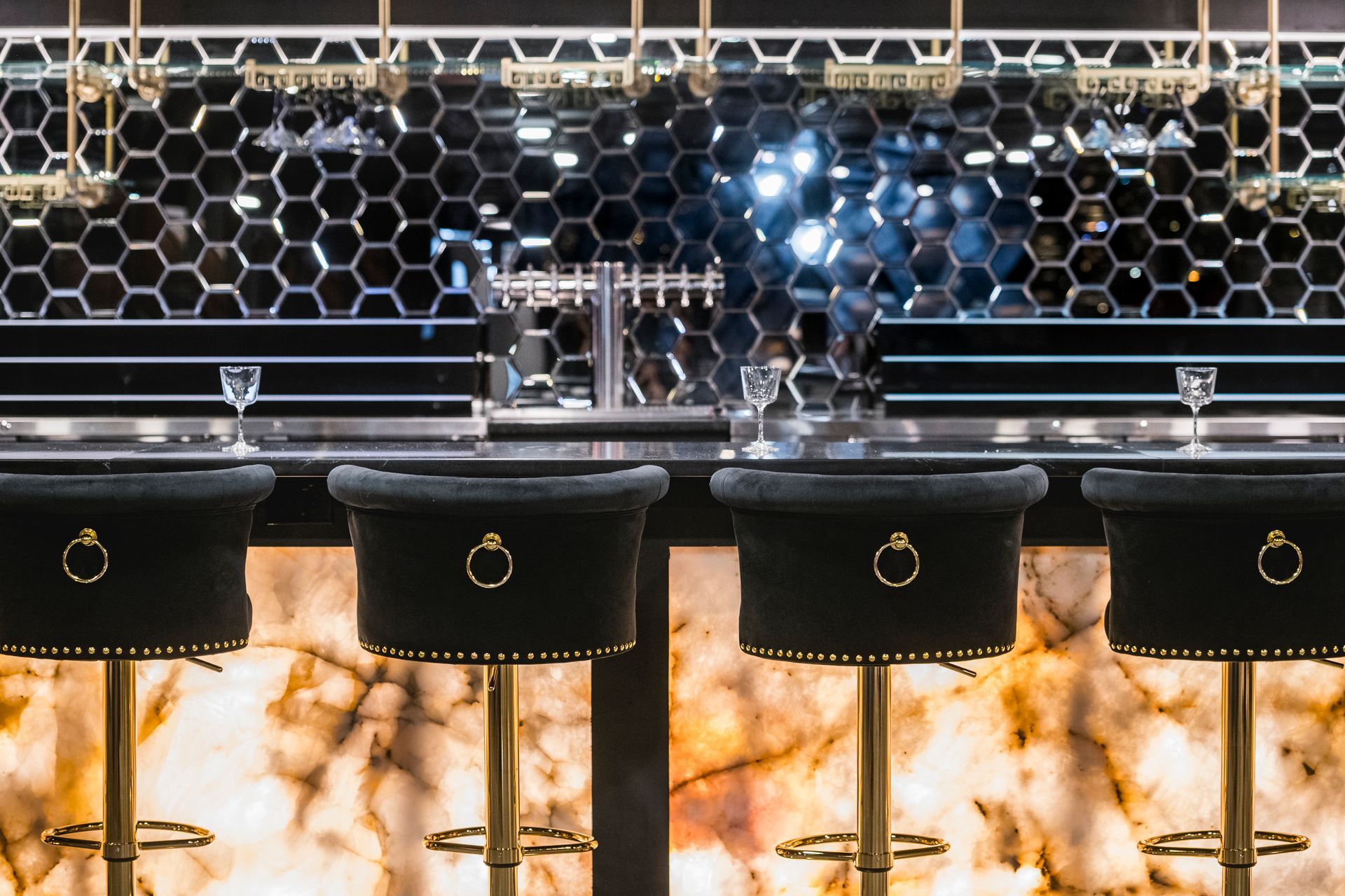 Modern bar with black sinks, gold fixtures, hex tile wall, and warm backlit stone counter